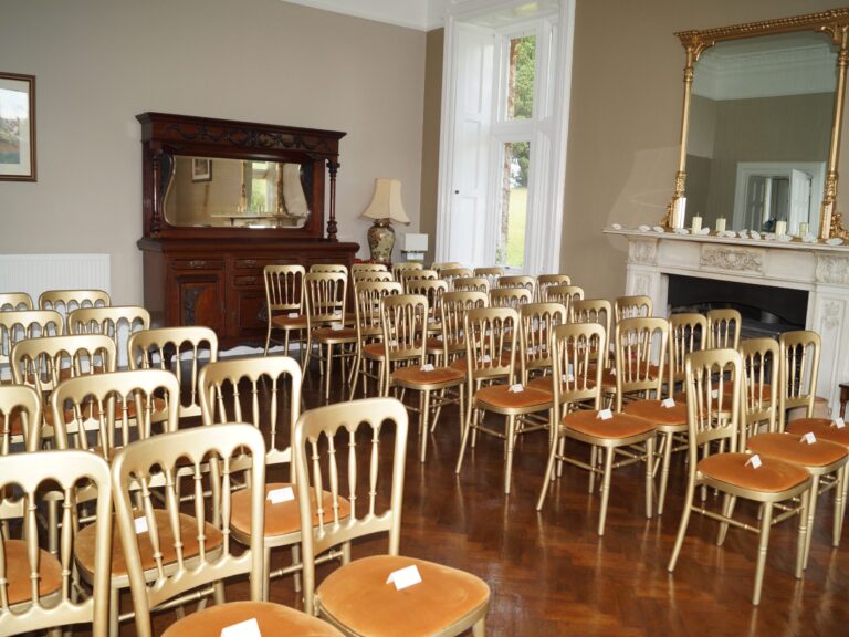 Rows of gold chairs facing a marble fireplace and gilt mirror, set for a smaller ceremony, Northcote Manor Hotel