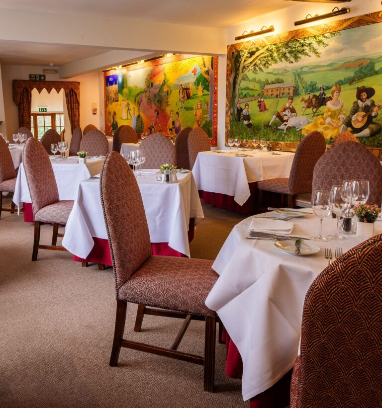 The restaurant laid for dinner, with high-backed chairs and large painted murals on the walls, Northcote Manor Hotel