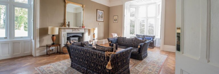 A lounge with patterned sofas, a marble fireplace and windows on two sides, Northcote Manor Hotel