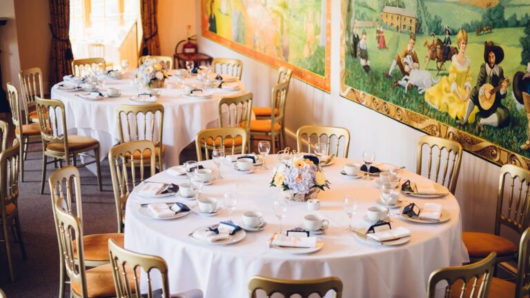 Round tables with white linen and gold chairs in the restaurant, beneath painted murals, Northcote Manor Hotel