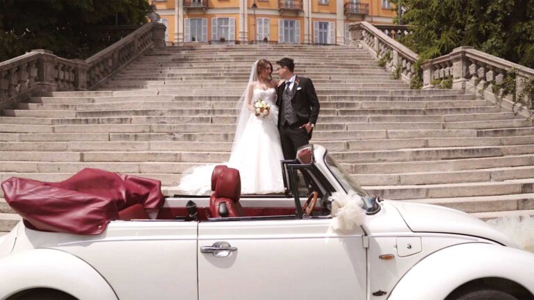 The couple on a palace staircase above a white convertible Beetle, Nozze da film
