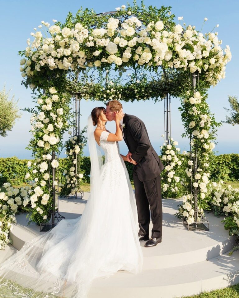 A couple kissing under a flower-covered arch, Nunta pe Plaja