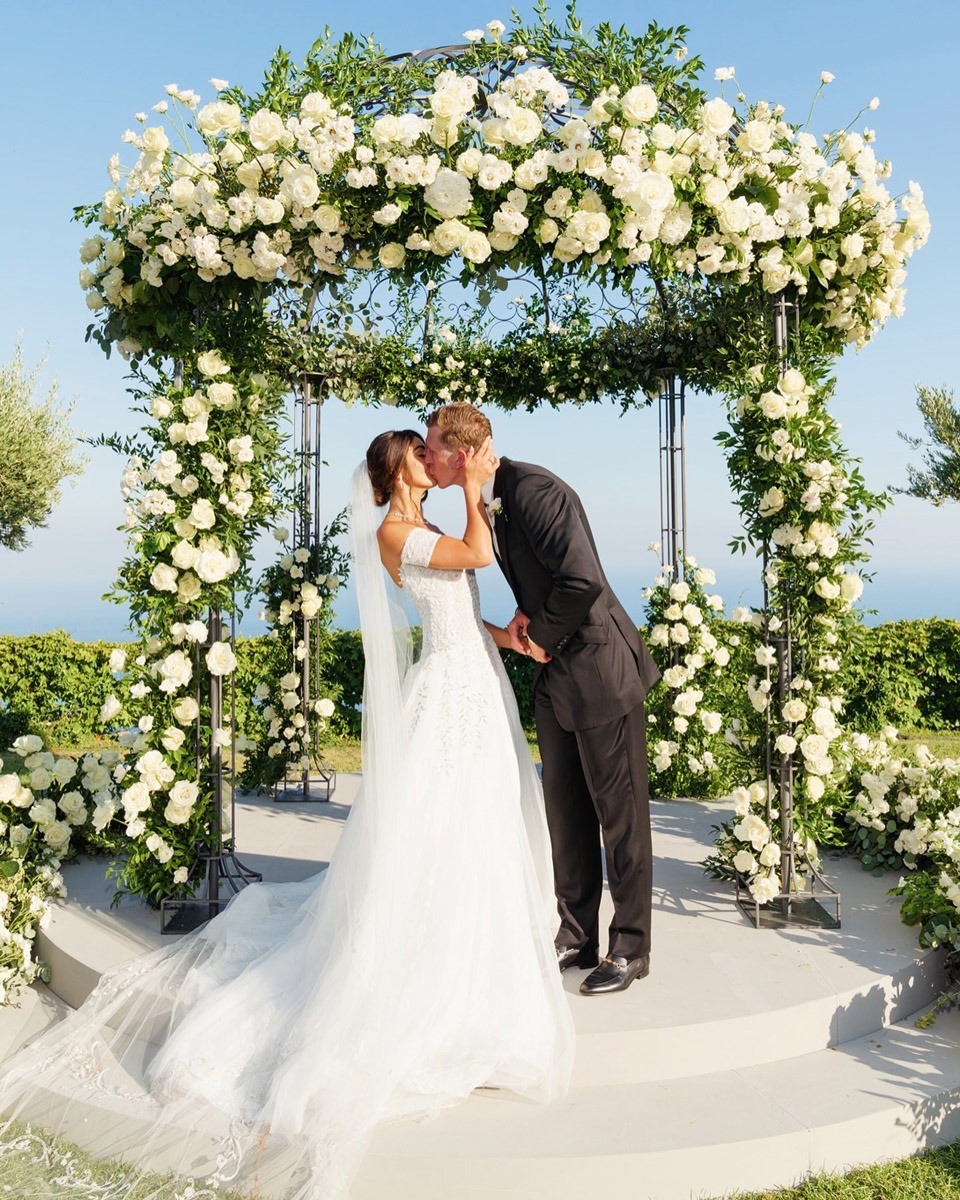A couple kissing under a flower-covered arch, Nunta pe Plaja