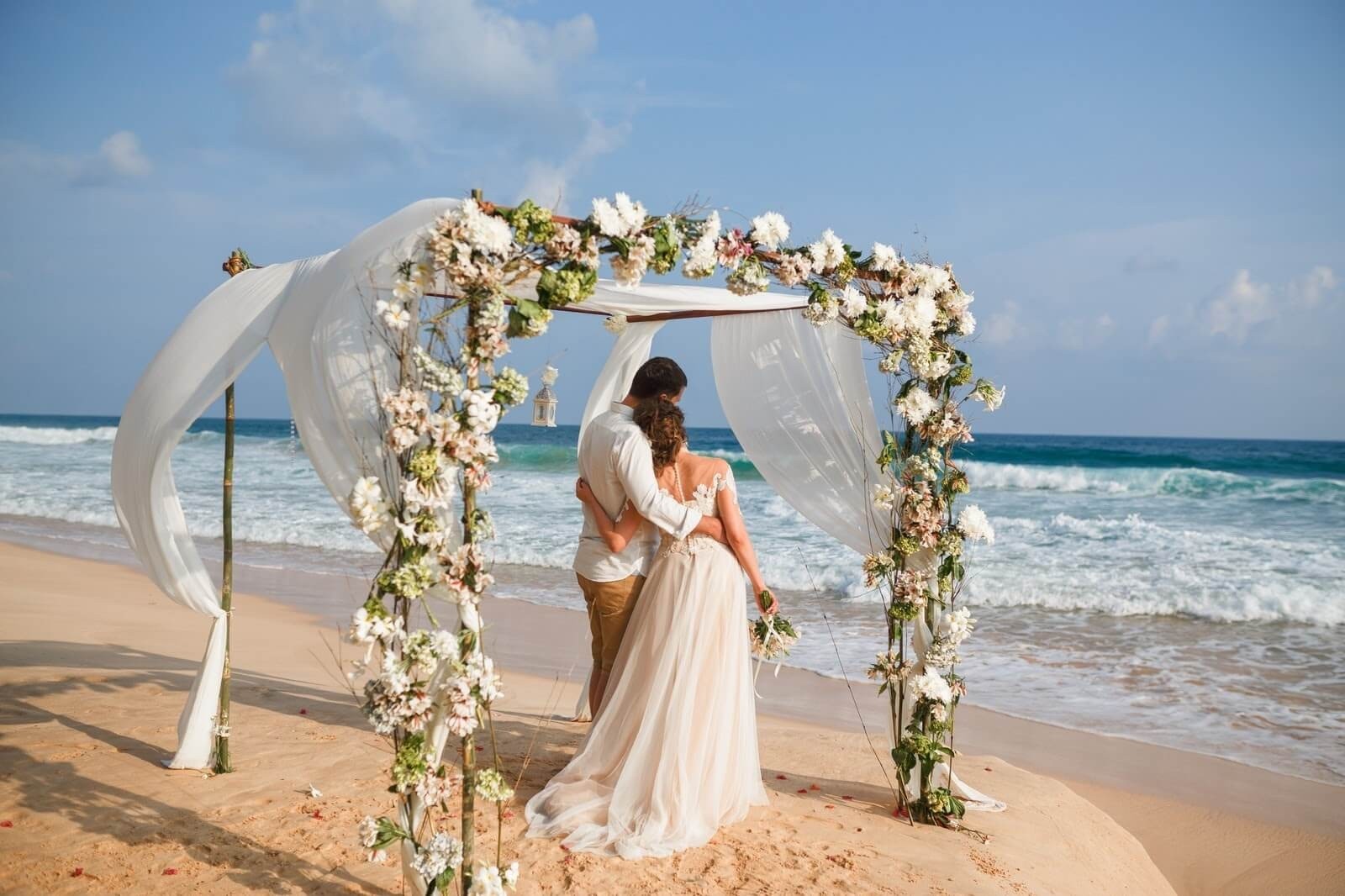 A couple under a floral arch on the beach, Nunta pe Plaja