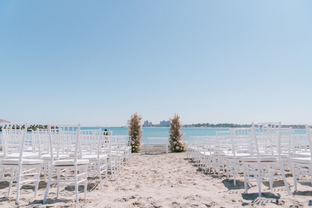 A beach ceremony aisle with white chairs leading to the sea, Nunta pe Plaja