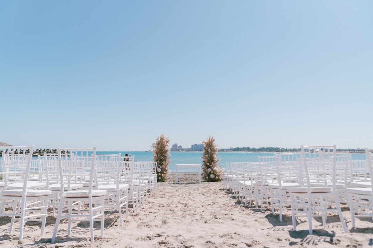 A beach ceremony aisle with white chairs leading to the sea, Nunta pe Plaja