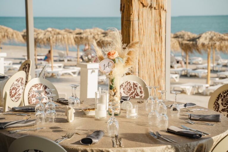 A beach reception table set under straw parasols, Nunta pe Plaja