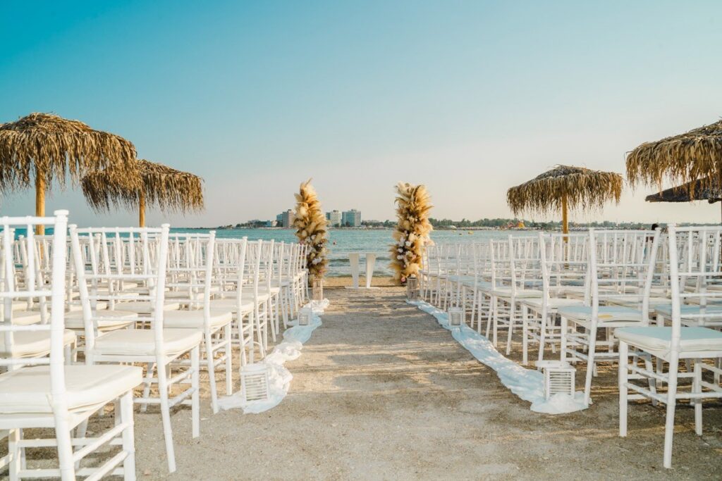 White chairs lined up along a wooden walkway by the sea, Nunta pe Plaja