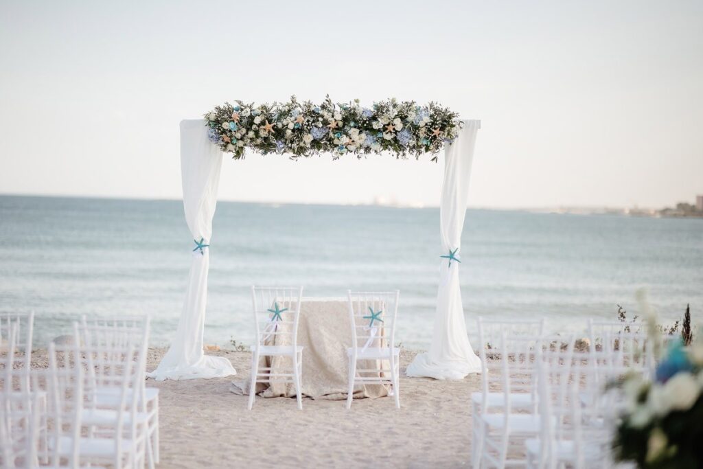 A white draped ceremony arch on the beach, Nunta pe Plaja