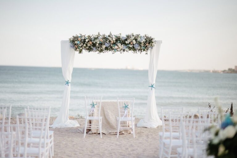 A white draped ceremony arch on the beach, Nunta pe Plaja
