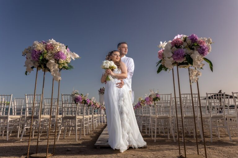 A bride and groom between tall floral stands on the beach, Nunta pe Plaja
