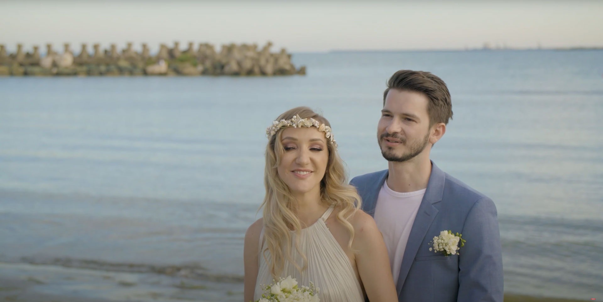 A bride and groom on the shore, her hair in a floral crown, Nunta pe Plaja