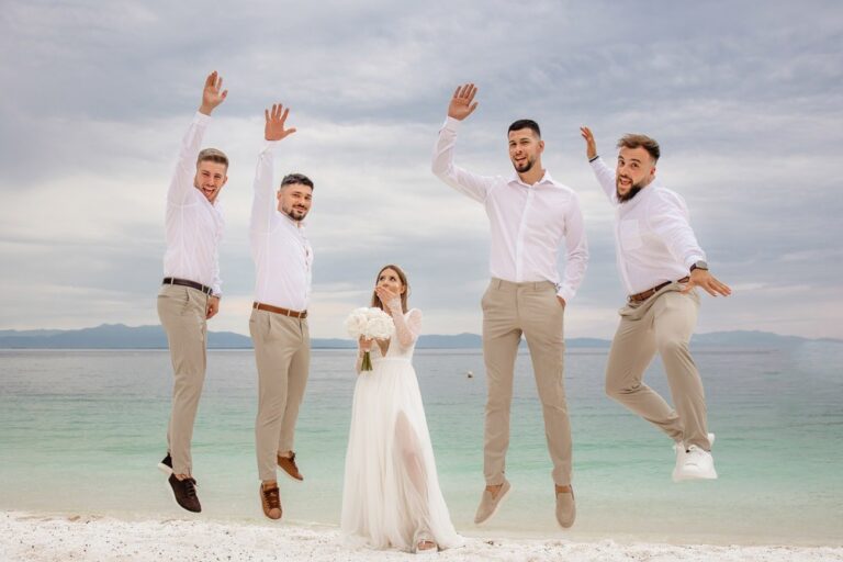 A groom and groomsmen jumping on a beach beside the bride, Nunta pe Plaja