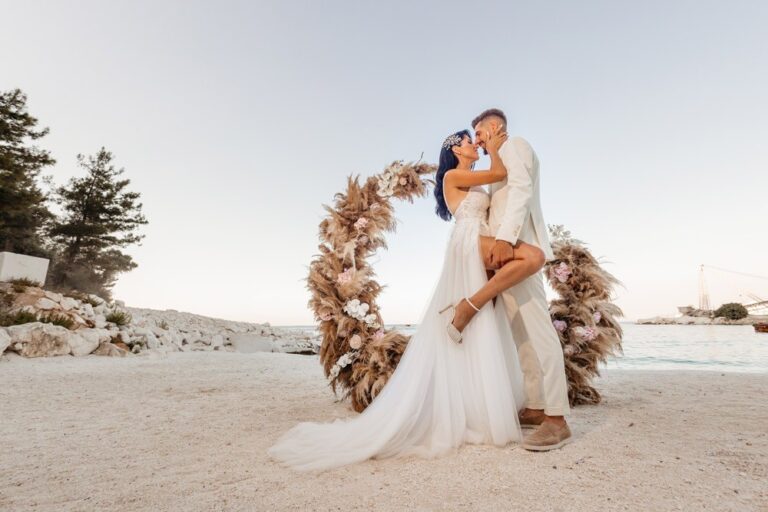 A couple in front of a dried-flower arch on the beach, Nunta pe Plaja