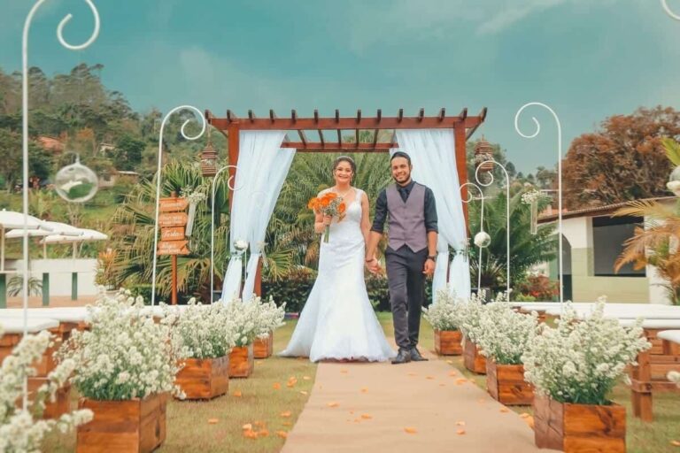 A couple walking down a garden aisle to a white canopy, Nunta pe Plaja