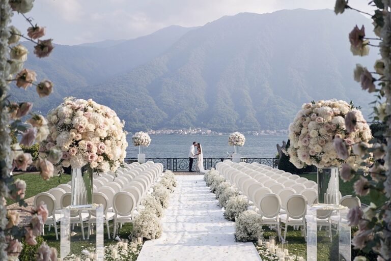 A lakeside ceremony with white chairs and flowers beneath mountains, Nunta pe Plaja
