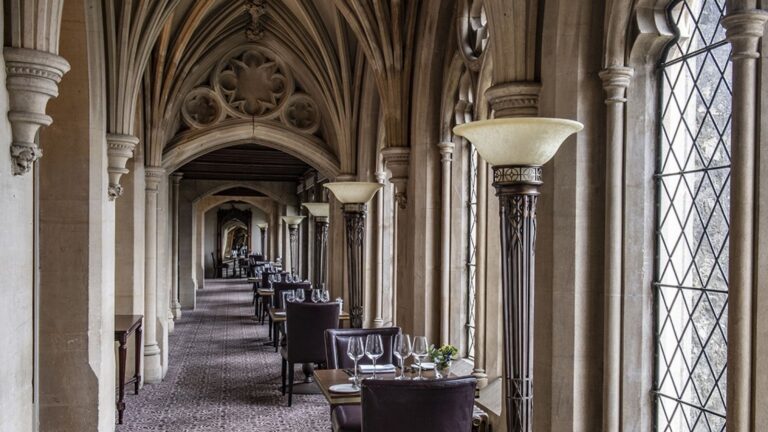The Cloisters, a vaulted Neo-Gothic stone gallery lined with arched windows and lamps, Nutfield Priory Hotel & Spa