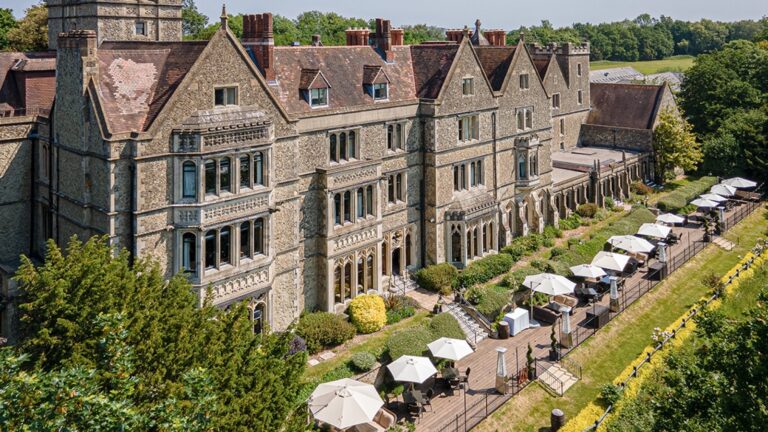 An aerial of the long mansion facade, the terrace and parasols running along the ridge, Nutfield Priory Hotel & Spa