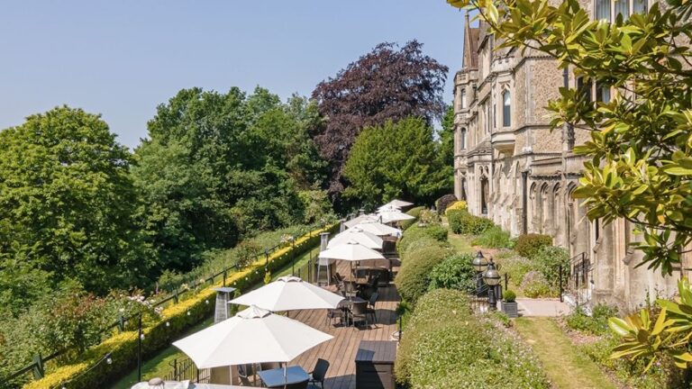 The sunlit south terrace, borders and parasols above the Surrey valley, Nutfield Priory Hotel & Spa