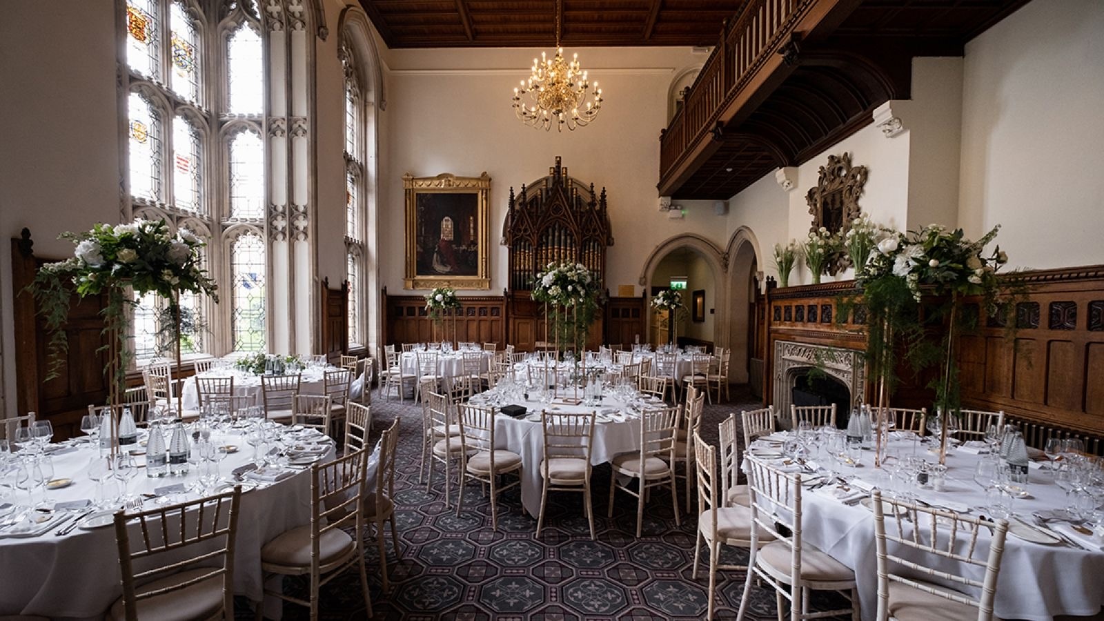 The galleried Great Hall dressed for a wedding breakfast, round tables beneath the minstrels' gallery and stained glass, Nutfield Priory Hotel & Spa
