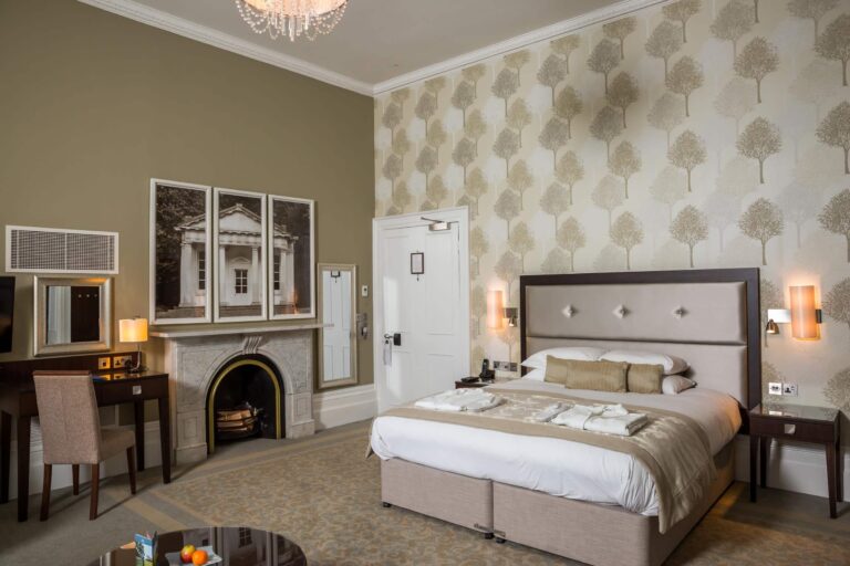 An Executive Bedroom with an original fireplace and patterned wallpaper, Oakley Hall Hotel