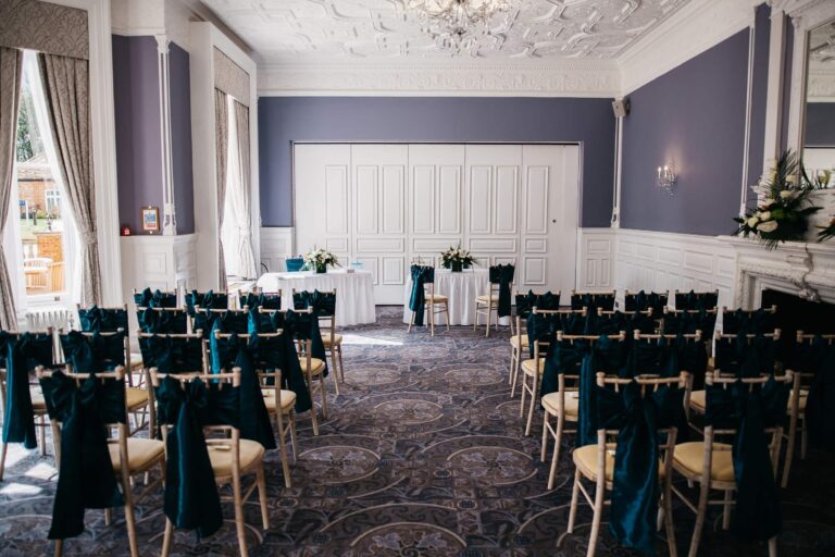 The Garden Room laid out for a ceremony with dark sashes on the chairs and a table at the window end, Oakley Hall Hotel