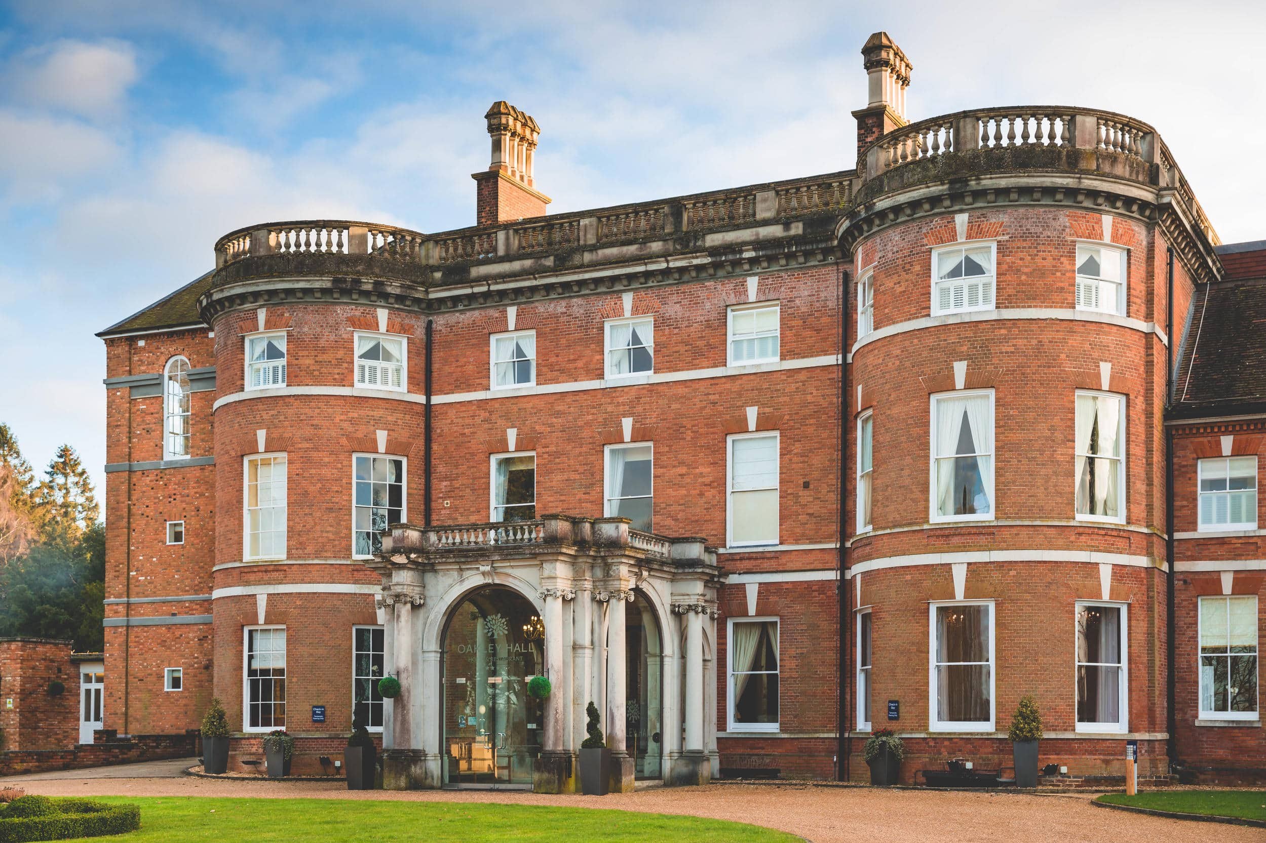 The entrance front, with its bowed bays, stone balustrade and arched porch over the drive, Oakley Hall Hotel
