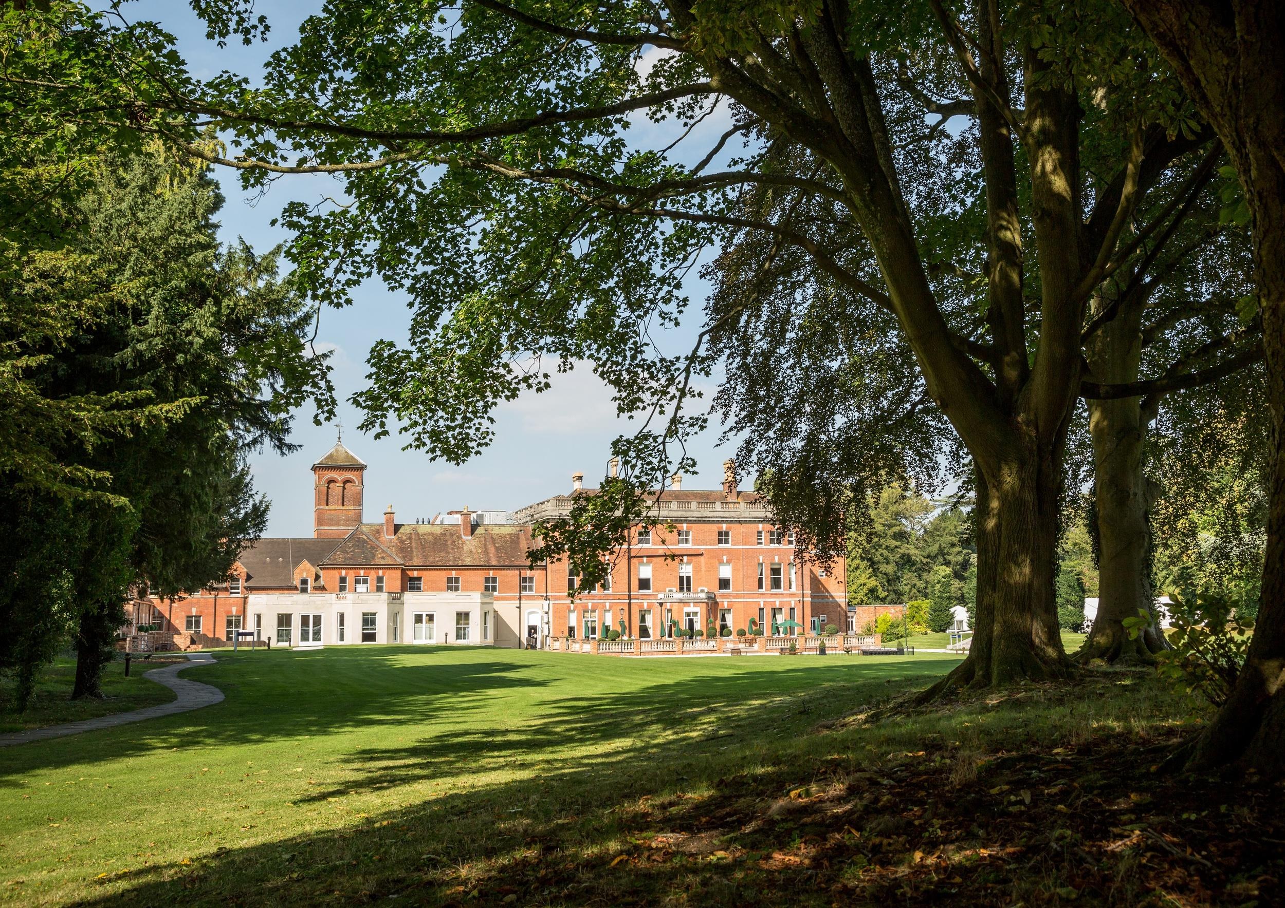 The house and clock tower seen from the shade of mature trees on the rear lawn, Oakley Hall Hotel