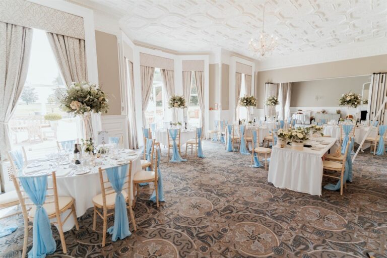 A room in the main house, likely the Garden Suite, dressed for a wedding breakfast with pale blue sashes and tall floral centrepieces, Oakley Hall Hotel