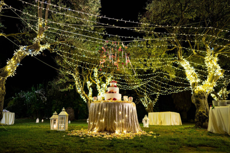 Wedding cake table under lit olive trees and festoon lights at night, Oggi Sposi & Events