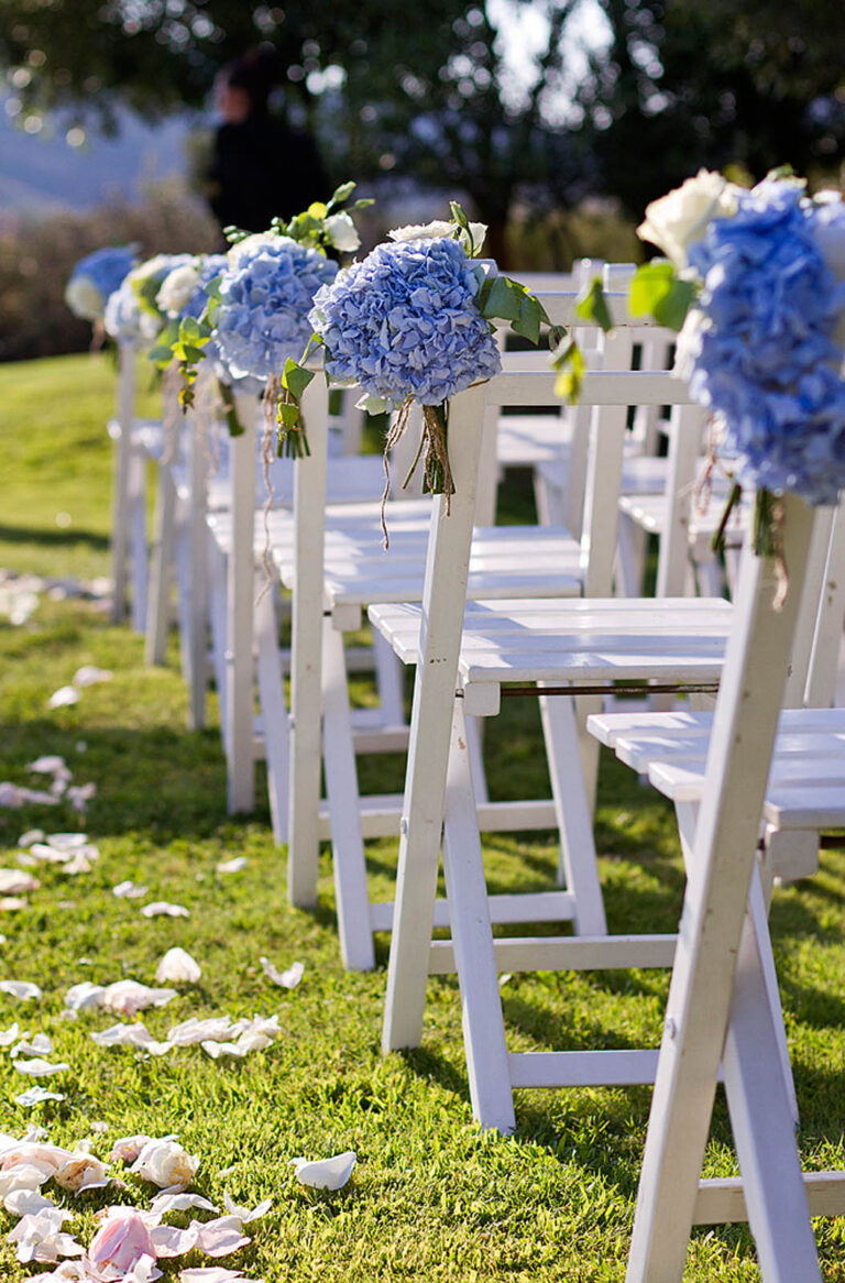 White garden chairs with blue hydrangeas along a petal-strewn aisle, Oggi Sposi & Events
