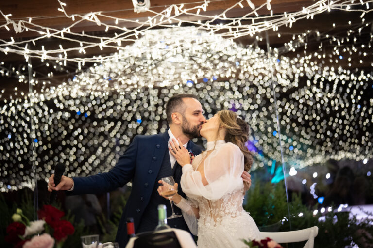 Couple kissing under a canopy of fairy lights at the reception, Oggi Sposi & Events