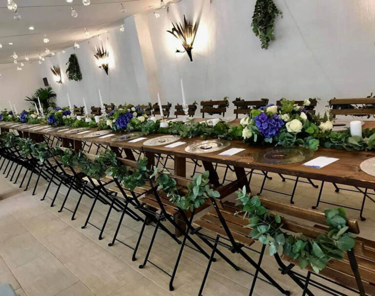 Long wooden tables with garlands of greenery and blue and white flowers, Oggi Sposi & Events