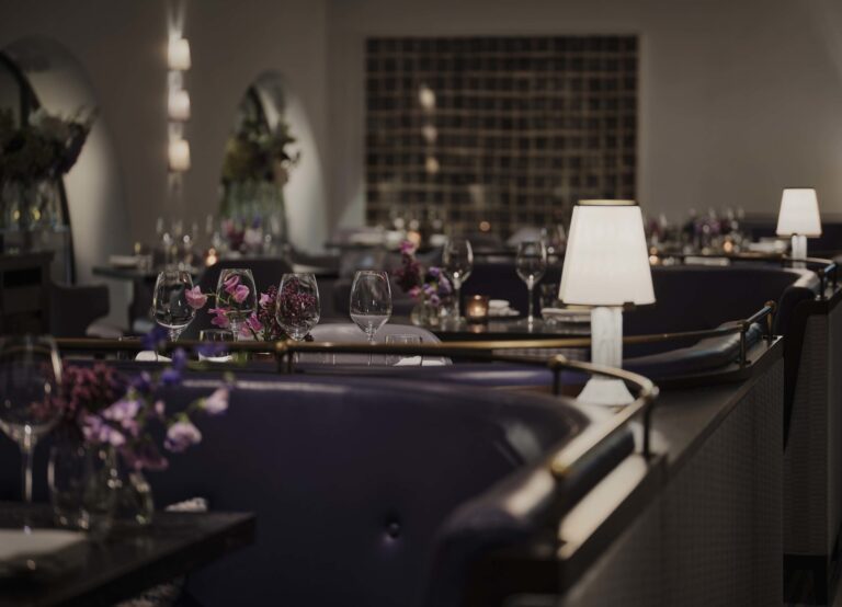 Indigo in the evening, with table lamps and flowers on tables set for dinner, One Aldwych