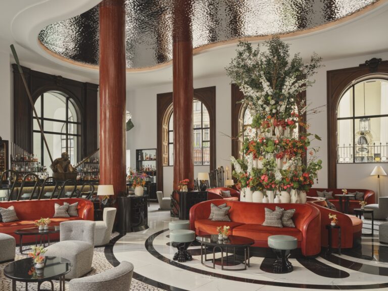The Lobby Bar under its double-height ceiling, with arched windows, red columns and a central flower display, One Aldwych