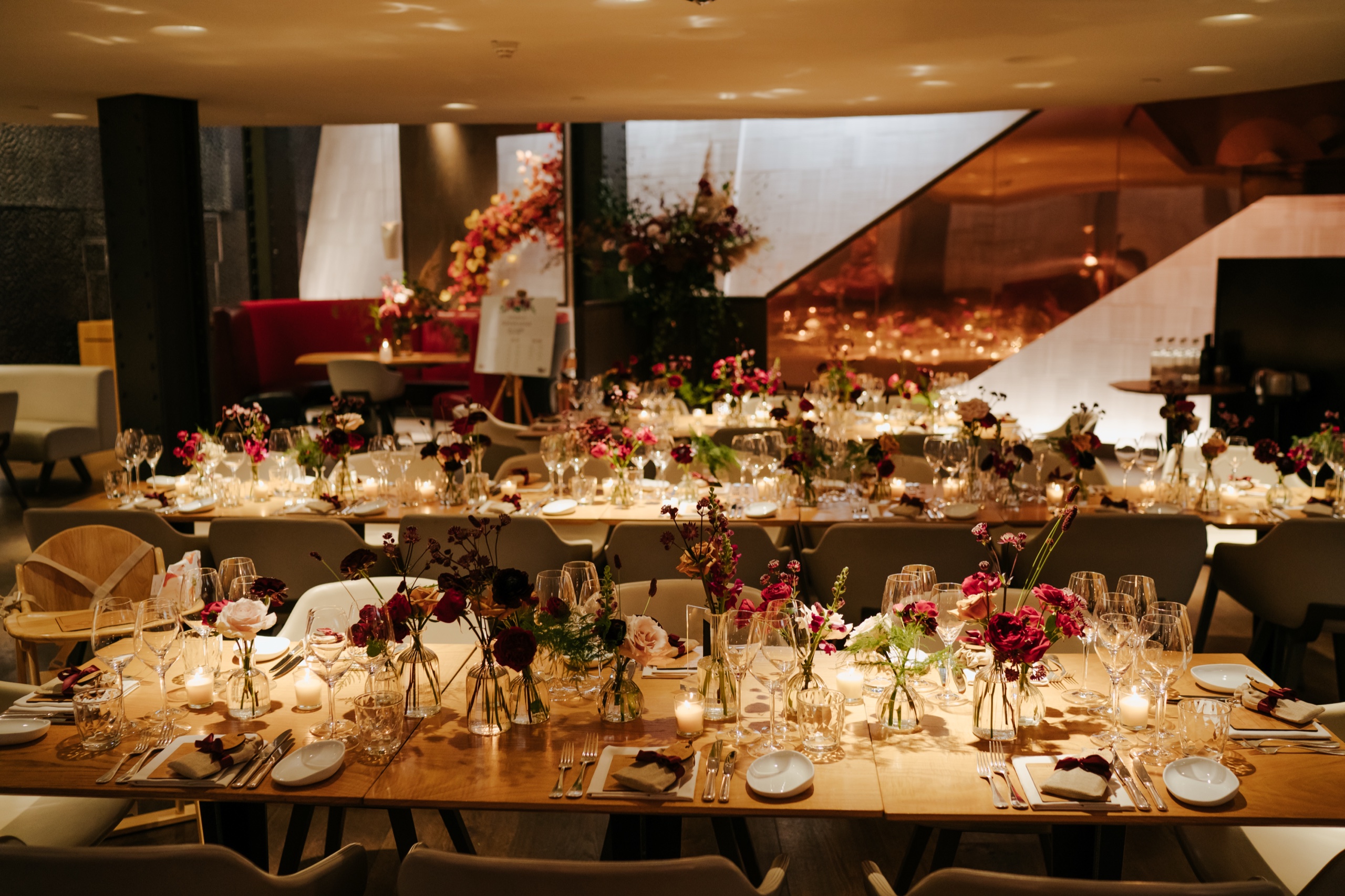 Downstairs at One Aldwych laid with long candlelit tables, bud vases of garden flowers and a seating plan by the copper staircase, One Aldwych