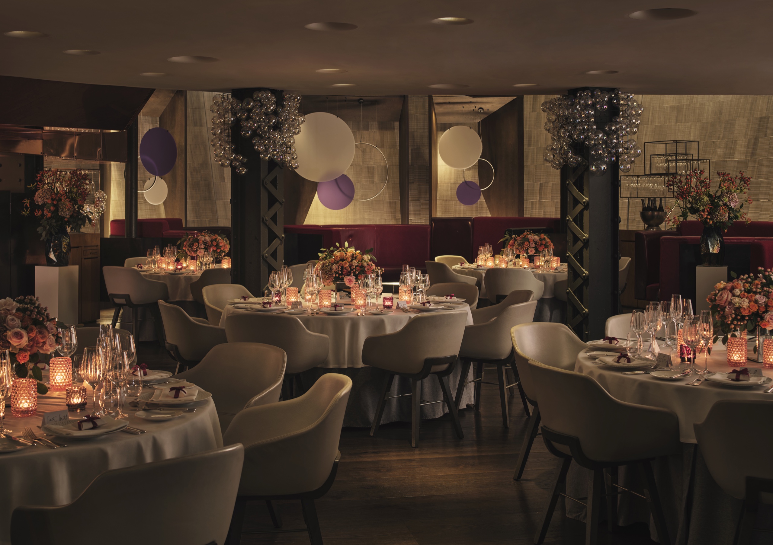 Round tables for a seated dinner on the lower-ground floor of Downstairs at One Aldwych, with floral centrepieces and candles, One Aldwych