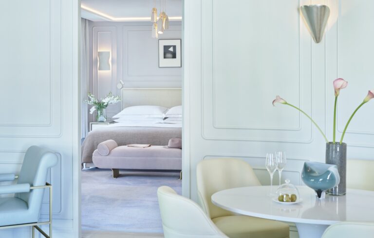An Aldwych Corner Suite, with a round dining table in the living room and the bedroom beyond, One Aldwych