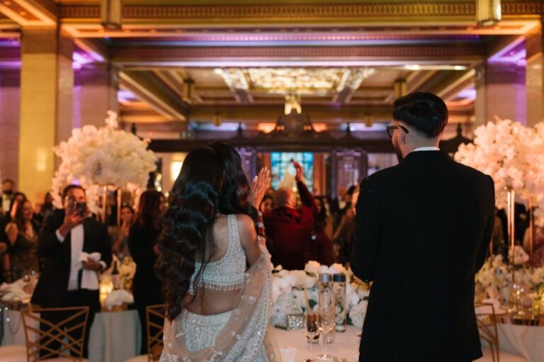 The bride in a beaded lehenga and the groom entering their reception between tall white orchid displays, One Marylebone