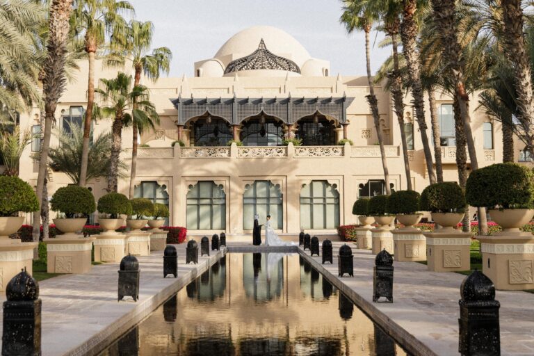 A couple at the end of a reflecting pool before the resort's arched facade, One&Only Royal Mirage