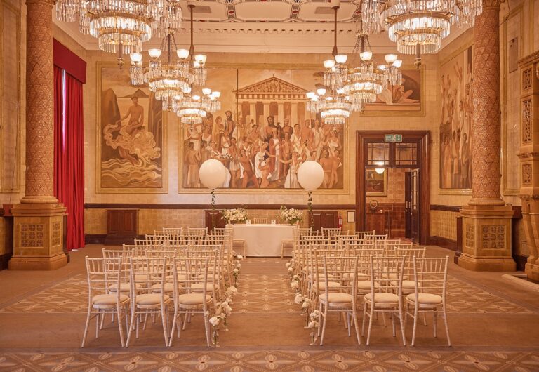 A ceremony laid out beneath chandeliers, facing a painted mural, One Whitehall Place