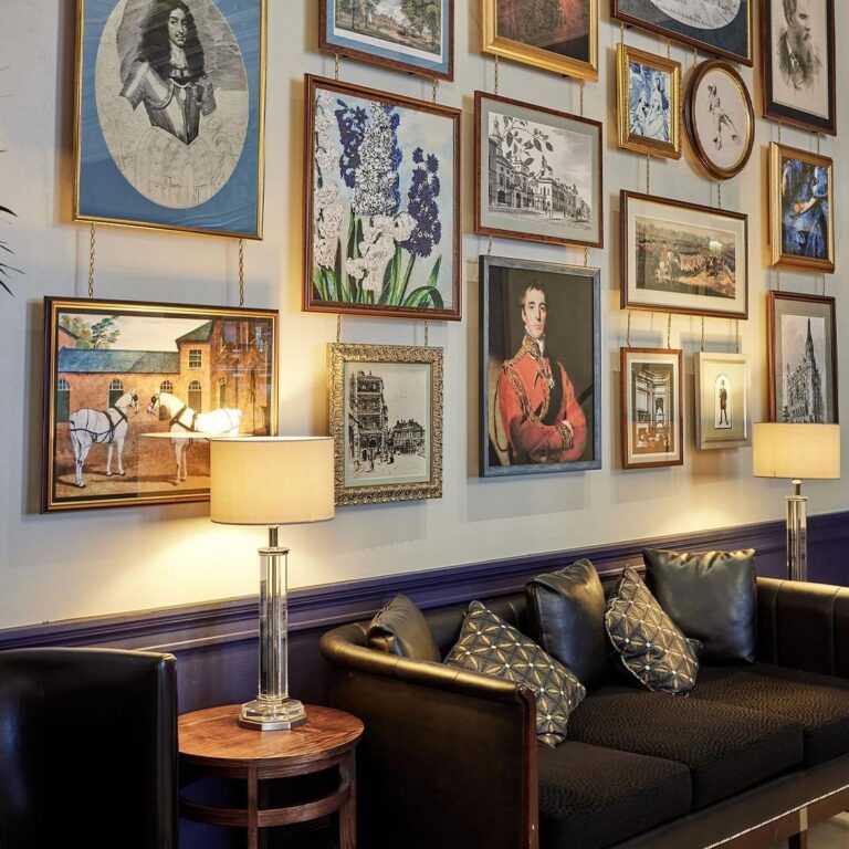 A wall of framed portraits beside a lamp and sofa, One Whitehall Place