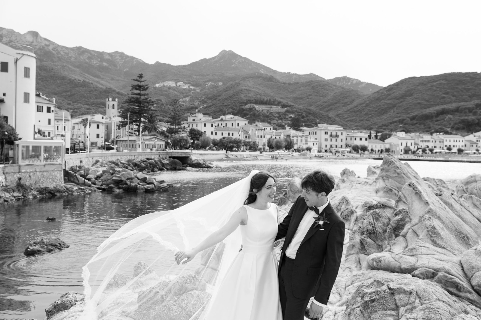 Bride and groom on the rocks above the harbour, veil in the wind, Isola d'Elba, black and white, Ordine della Giarrettiera