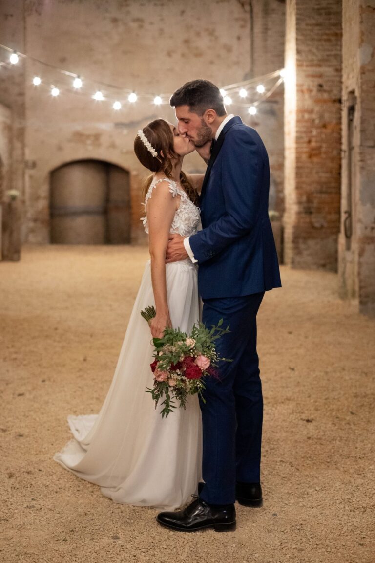 A kiss beneath string lights in the courtyard of Cascina Lago Scuro, Ordine della Giarrettiera