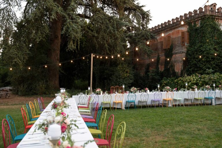 A long table with coloured chairs under strings of lights, Cascina Lago Scuro, Ordine della Giarrettiera