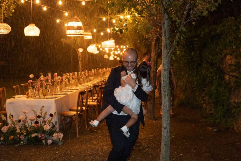 A guest carrying a child past the long table under hanging lanterns, the same evening the storm broke, Ordine della Giarrettiera