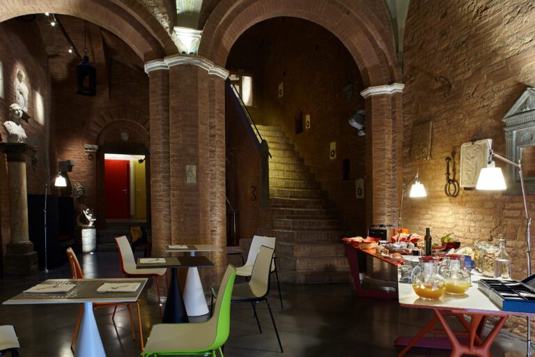 A stone-vaulted hall with a staircase, laid for dining, Palazzetto Rosso