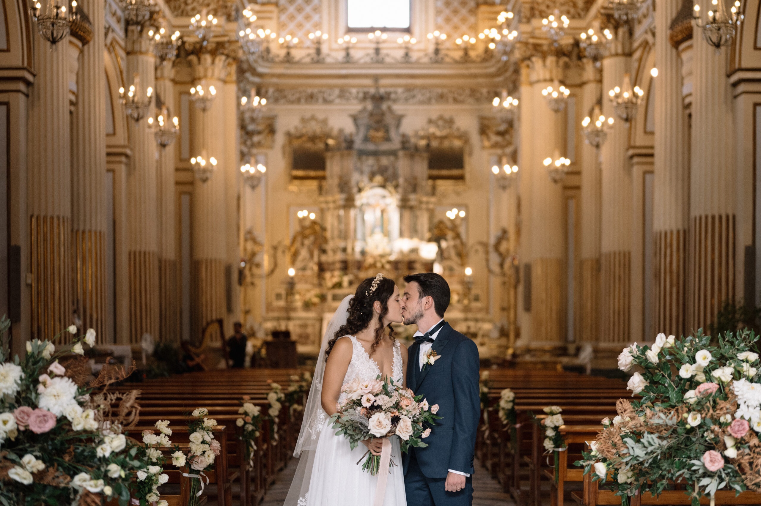 A baroque church, gilt and chandeliers, the kiss in the aisle between two urns of roses, Pangiunìa Wedding
