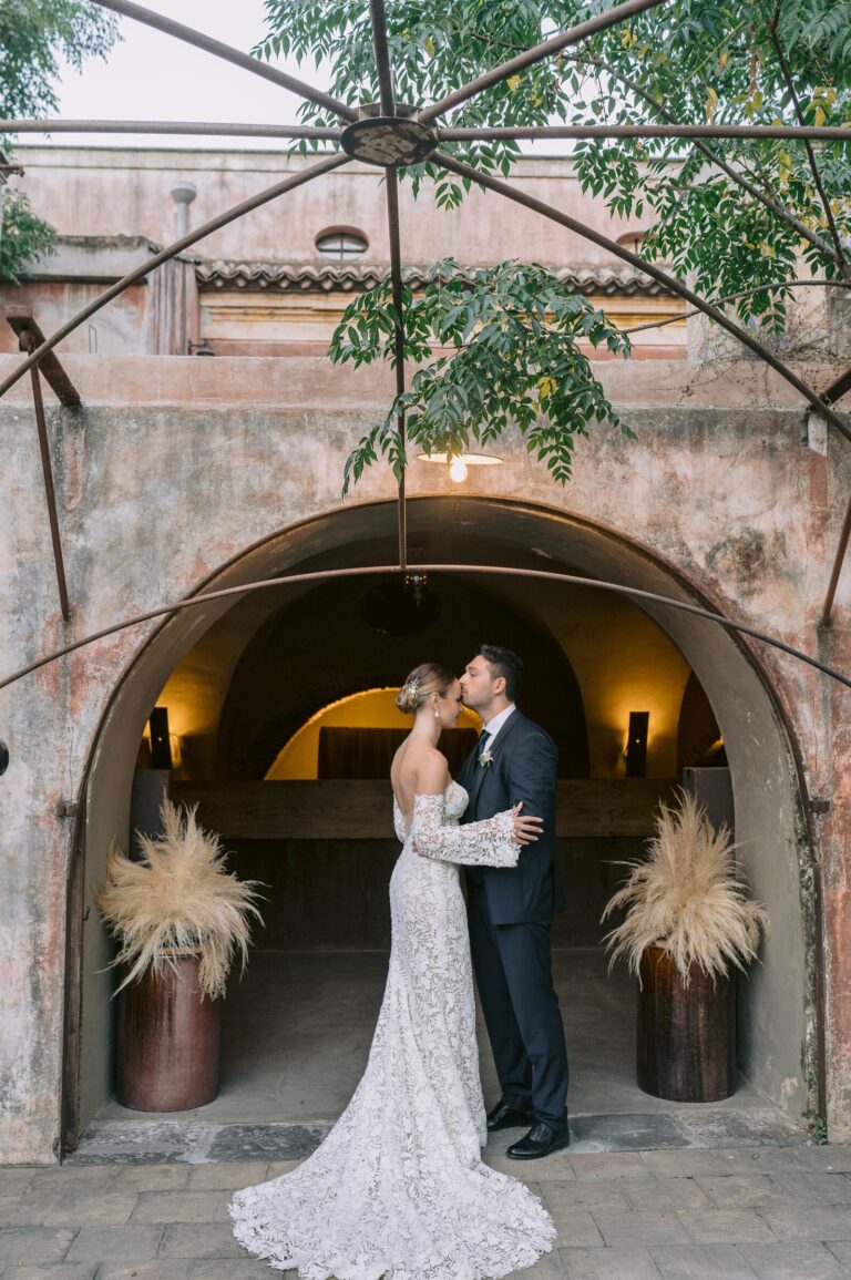 The kiss under a farm arch, two bronze urns of pampas either side, Pangiunìa Wedding