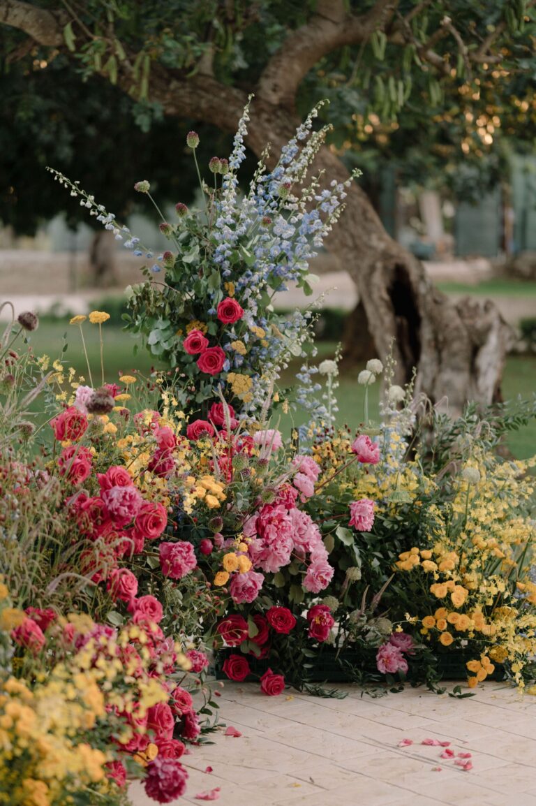 The same florals built around the trunk of an old olive tree, petals on the paving, Pangiunìa Wedding